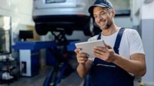 Happy auto repairman working on touchpad in a workshop Happy auto repairman working on touchpad in a workshop