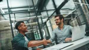 welcome-on-board-two-young-and-handsome-men-shaking-min Welcome on board Two young and handsome men shaking hands and smiling while working in modern office